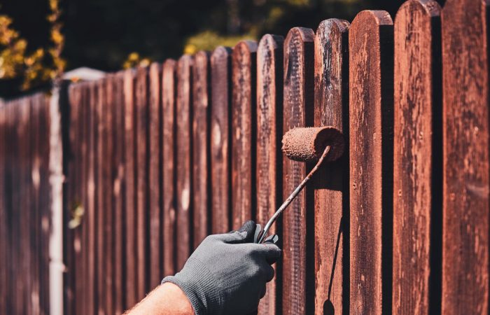 man-protective-gloves-is-painting-wooden-fence-bright-summer-day